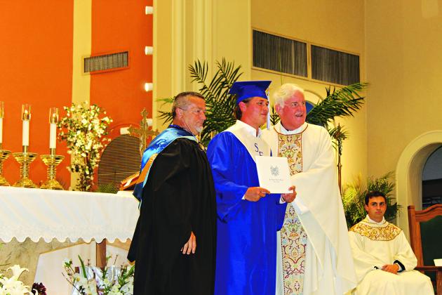 Joseph Ryan Young receives his high school diploma from his Principal Mitchell Fontenot and the Rev. Hampton Davis Saturday morning during the school’s graduation Mass ceremony.