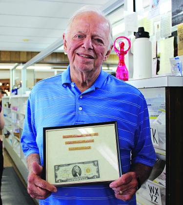 Augie Courville holds a framed $2 bill. It reads, “First purchase made by Aaron Frank McGee, July 29, 1974.”  Courville said McGee purchased a box of Pangburn’s chocolates. (Photo by Myra Miller)