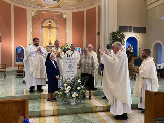 From left, are the Rev. William Schambough, the Rev. Randy Moreau, the Rev. Paul LaFleur, the Rev. Henry Broussard, the Rev. Raymond Ssebina Musisi, the Rev. Hampton Davis, and the Rev. Nick Ware. In front by the plaque are Sister Nell Murray and Sister Joel Miller.