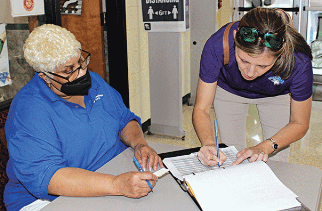 Dana Landry signs her name on the voting registery at Eunice High School Tuesday afternoon. Debra Gallien, a commissioner, assists her. (Photo by Myra Miller)