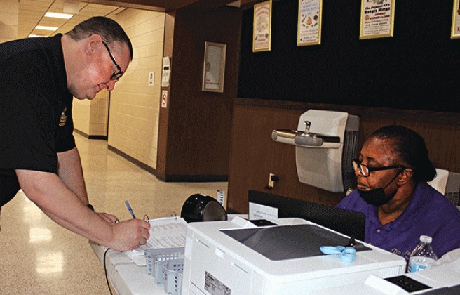 James M. Guidry signs his name at early voting at the City Hall on Tuesday. Assisting him is Cynthia Martin, commissioner. (Photo by Myra Miller)