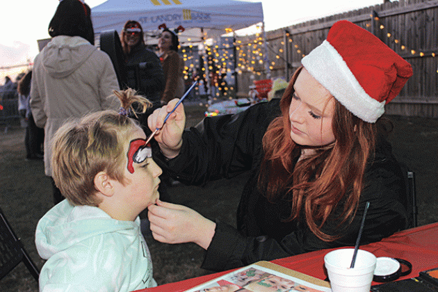Josephine Rodriguez paints a Santa hat on the face of Henry Kyzar, 7, at the Christmas Festival.