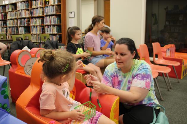 Katlin Manuel assists her daughter Evangeline Manuel, 5, with a Friendship necklace at Story Time hour Wednesday.