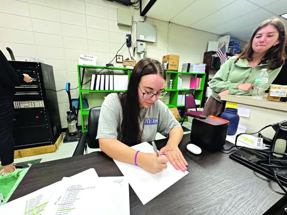 Lainey Fruge, 17, of Eunice High School, writes her name in cursive, while classmate Kelsie  Gaspard, 18, watches. Both students said they only know how to write their names in cursive. (Photo by Rebecca Chaisson)