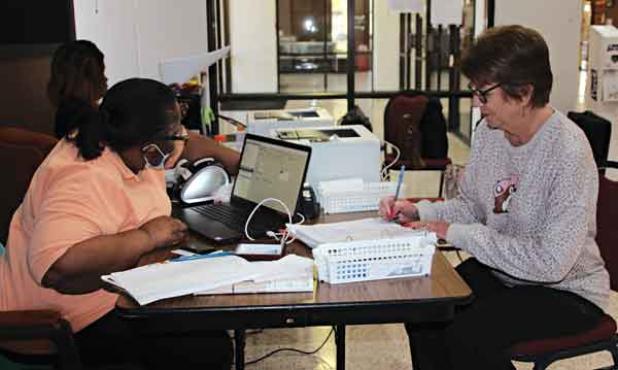 Joan Richard signs her name before she casts her vote Wednesday morning at the Eunice City Hall. Early voting continues through Saturday at the Eunice City Hall. Working the elections at the table were Cynthia Martin, left, and Trovette  Martin. (Photo by Myra Miller)