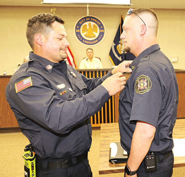 Chaise Brown, right, receives his badge as Eunice fire chief from his brother Ben Brown, a Eunice firefighter/operator, at Tuesday’s Board of Aldermen meeting. In the background is Mayor Scott Fontenot. (Photo by Harlan Kirgan)