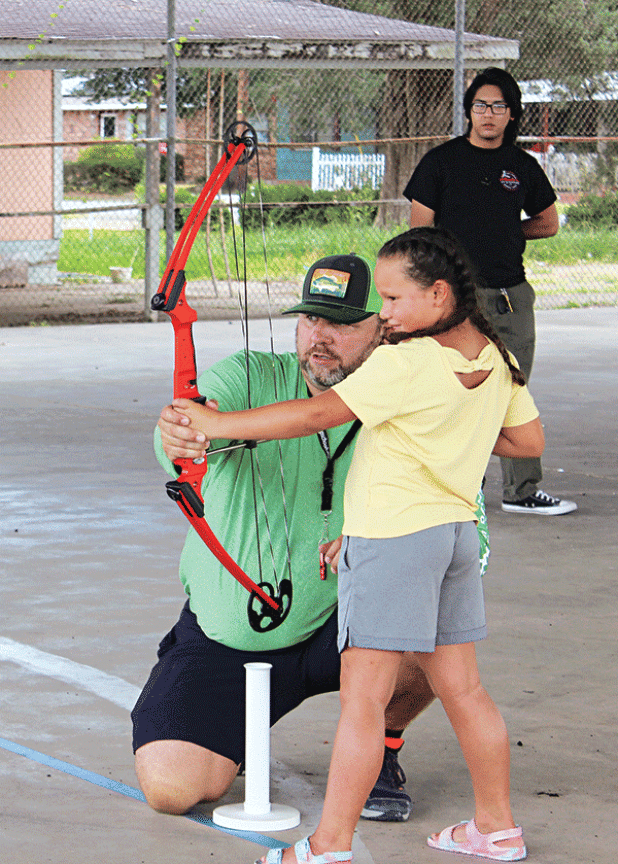 Gabby Briannez, 7, holds her concentration as Eunice Recreational Director Robert Johnson shows her some archery skills during an archery summer camp held at the Southeast Center pavilion. (Photo by Myra Miller)