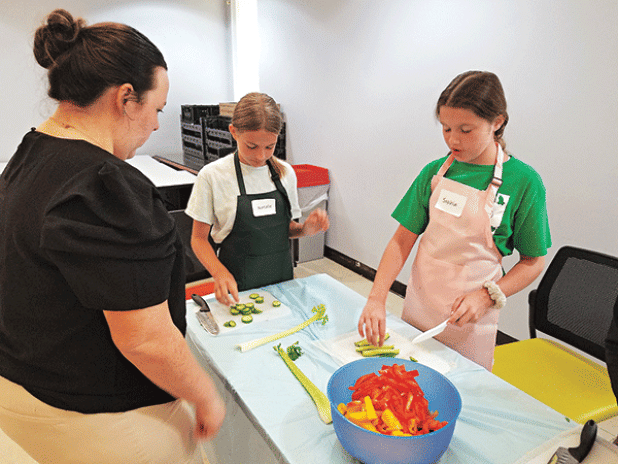 Emmerson Lyons, LSU AgCenter 4-H intern in St. Landry Parish is supervising Kid Chef Camp participants, Natalie Arceneaux, left, and Sophia Benoit, right, practicing their knife skills by cutting vegetables. (Photo by Lisa Benoit/LSU AgCenter)