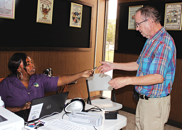 Trovette Matt, an employee with the Registrar’s of Voters Office, hands back Marcus N. Fontenot’s drivers license Tuesday morning at Eunice City Hall during early voting. (Photo by Myra Miller)