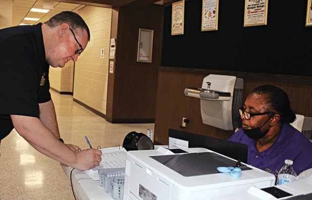 James M. Guidry signs his name at early voting at the City Hall on Tuesday. Assisting him is Cynthia Martin, commissioner. (Photo by Myra Miller)