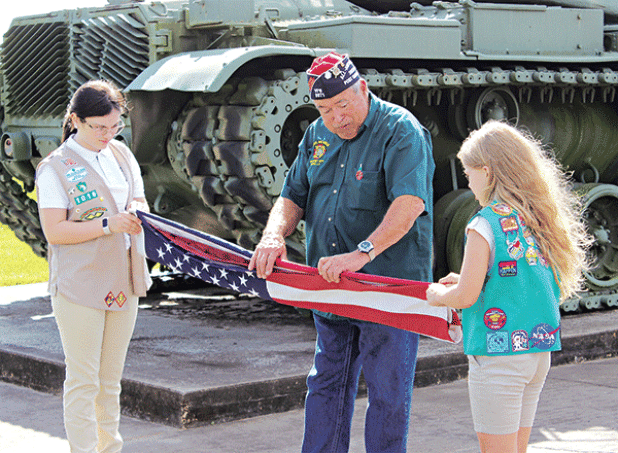 Girl Scout Troop 1016 members  Ava Ortego, left, and Kallie Bakka performed the flag-raising ceremony during the Veterans Day program held at the VFW 8971 Post Hall. Showing the two scouts the proper flag folding etiquette is Bob Witkovski, VFW Post 8971 quartermaster. Turn to Page 12 for additional Veterans Day photos. (Photo by Myra Miller)