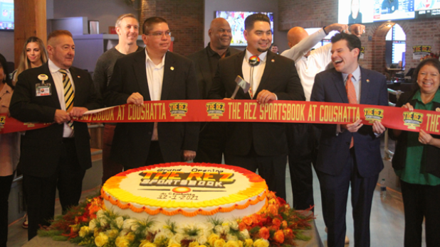 Flanked by members of the Coushatta Tribal Council Crystal Williams, Kristian Poncho, Loretta Williams, and Kevin Sickey, Chairman Jonathan Cernek (center) cuts the ribbon at the grand opening of The Rez Sportsbook in Kinder. From left, in the back, are former NFL players Owen Daniels, Rickey Jackson and Drew Pearson. (Ville Platte Gazette photo by Tony Marks)