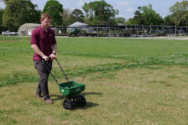 Eric DeBoer, an assistant professor of turfgrass management with the LSU AgCenter, demonstrates using a spreader to apply fertilizer. (Photo by Randy LaBauve/LSU AgCenter)
