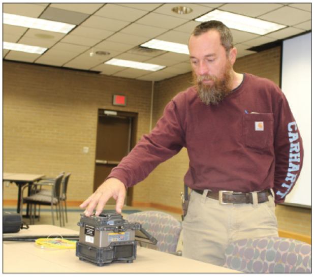 Kenny Miller is next to a fusing machine. A fusing machine he has is for fiber optic. Miller said, “It goes through and takes your fiber optic glass, fuses and welds it together and makes a connection, and this can be used for video, and internet.” Miller was the Rotary Club’s guest speaker Wednesday. He was the guest of Alex Morris. (Photo by Myra Miller)
