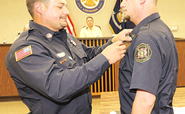 Chaise Brown, right, receives his badge as Eunice fire chief from his brother Ben Brown, a Eunice firefighter/operator, at Tuesday’s Board of Aldermen meeting. In the background is Mayor Scott Fontenot. (Photo by Harlan Kirgan)