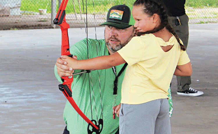 Gabby Briannez, 7, holds her concentration as Eunice Recreational Director Robert Johnson shows her some archery skills during an archery summer camp held at the Southeast Center pavilion. (Photo by Myra Miller)