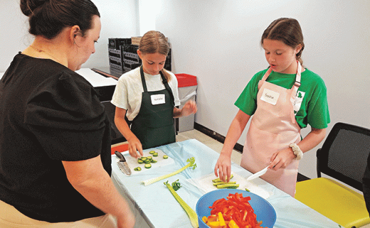Emmerson Lyons, LSU AgCenter 4-H intern in St. Landry Parish is supervising Kid Chef Camp participants, Natalie Arceneaux, left, and Sophia Benoit, right, practicing their knife skills by cutting vegetables. (Photo by Lisa Benoit/LSU AgCenter)