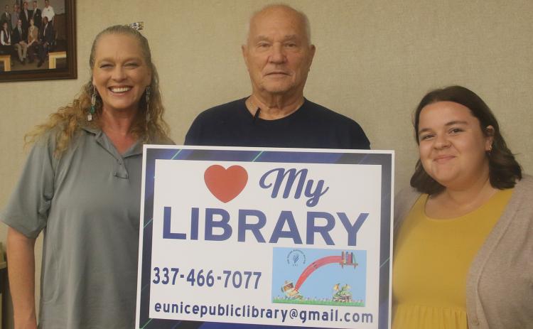 The Friends of the Eunice Public Library is selling yard signs promoting the library for $15 each. The signs, which were introduced at Tuesday’s Eunice city council meeting,  are available at the library. Holding a yard sign are, from left, Jena Donaldson, children’s program librarian; Tony Baltakis, president of the Library Board of Control; and Allison Duplechain, librarian. (Photo by Harlan Kirgan)