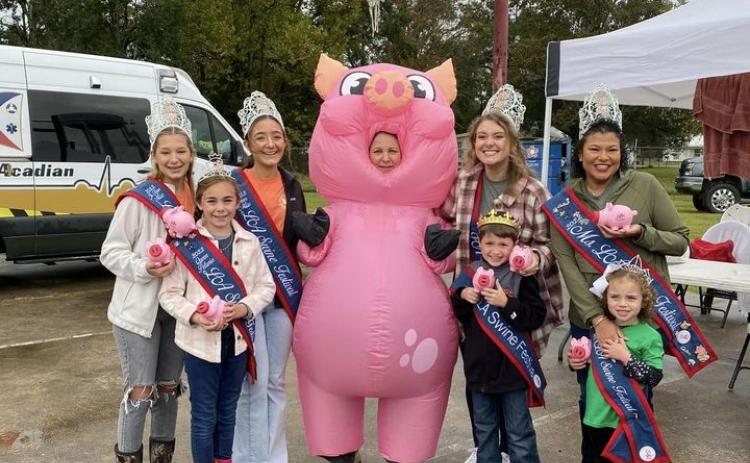 Swine Festival royalty enjoying last year’s event is seen above. From left, are,  Ava Manuel, Mallory Ortego, Bailey Stelly, Champion Hog Caller Jackie Ravey in the pig costume, Abigail Fruge, Carson Johnson, Vanessa Lastrapes, and Skyla McElfresh.  (Submitted photo)
