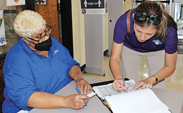 Dana Landry signs her name on the voting registery at Eunice High School Tuesday afternoon. Debra Gallien, a commissioner, assists her. (Photo by Myra Miller)