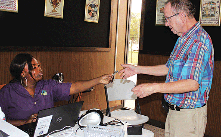 Trovette Matt, an employee with the Registrar’s of Voters Office, hands back Marcus N. Fontenot’s drivers license Tuesday morning at Eunice City Hall during early voting. (Photo by Myra Miller)