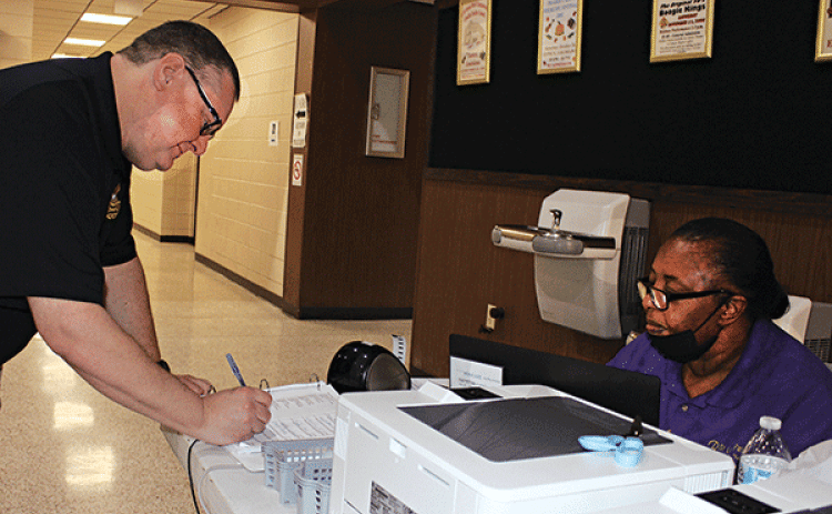 James M. Guidry signs his name at early voting at the City Hall on Tuesday. Assisting him is Cynthia Martin, commissioner. (Photo by Myra Miller)